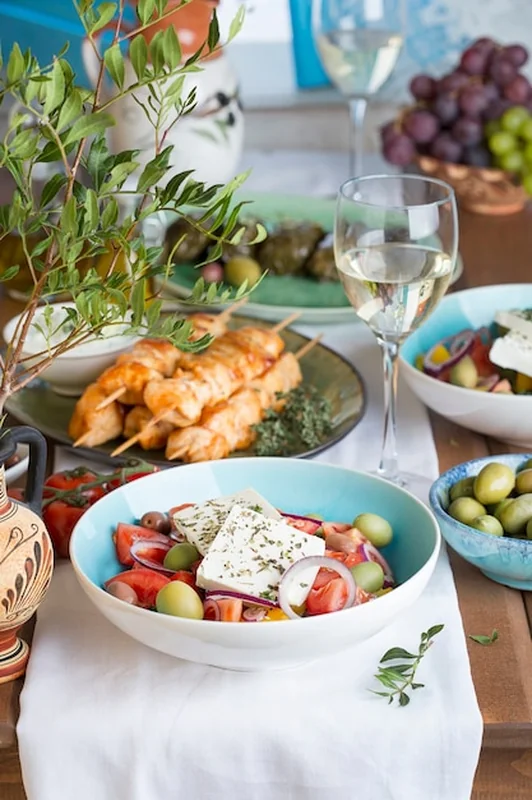 Tradycyjny grecki obiad na dużym stole: sałatka z fetą, souvlaki, oliwki i wino