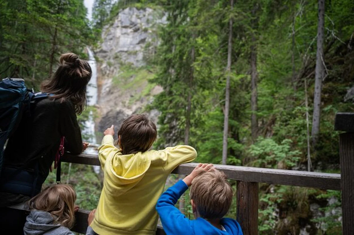 Młoda matka z trójką dzieci obserwująca wodospad w letniej przyrodzie