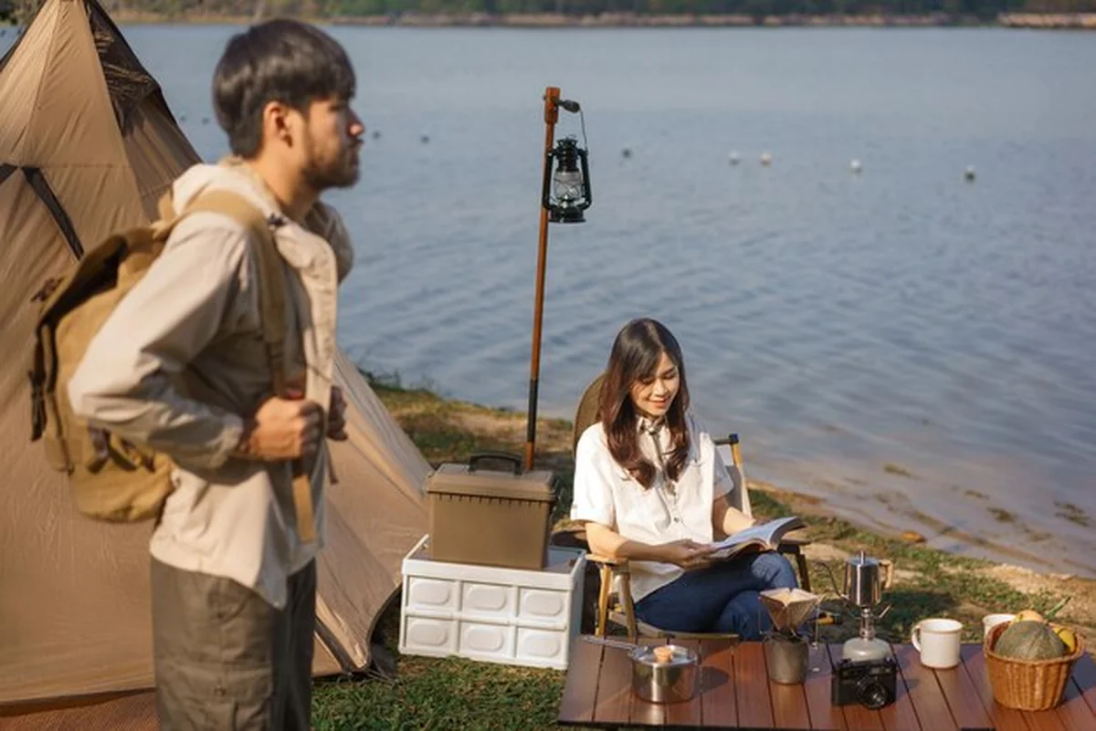 Młoda para aktywna poza namiotem, czytająca książkę i podziwiająca jezioro