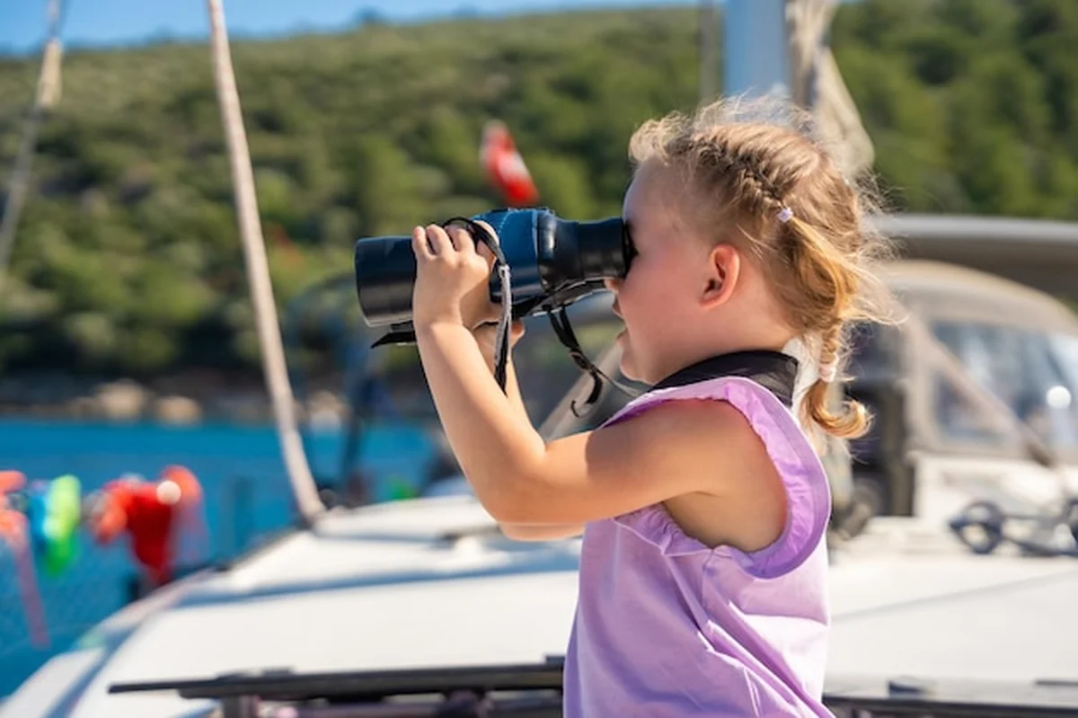 Mała dziewczynka patrząca przez lornetkę na jachcie w morzu